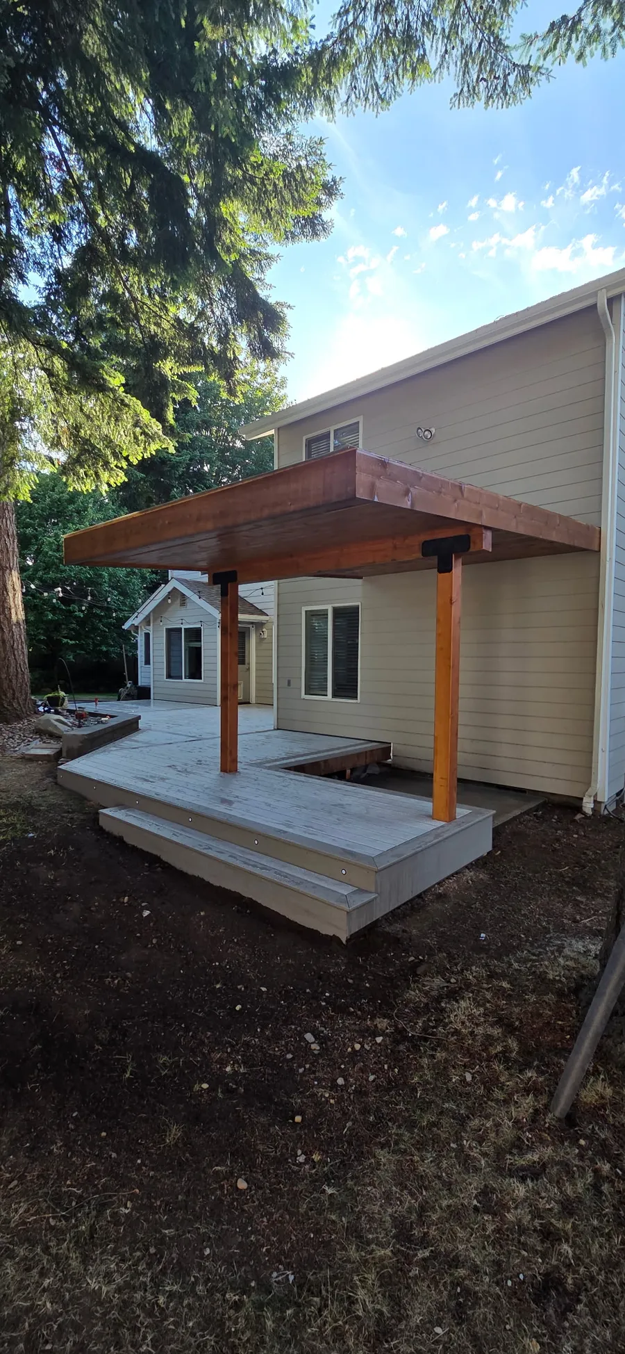 Backyard deck with a cedar-framed covered roof on two posts, attached to a tan sided home