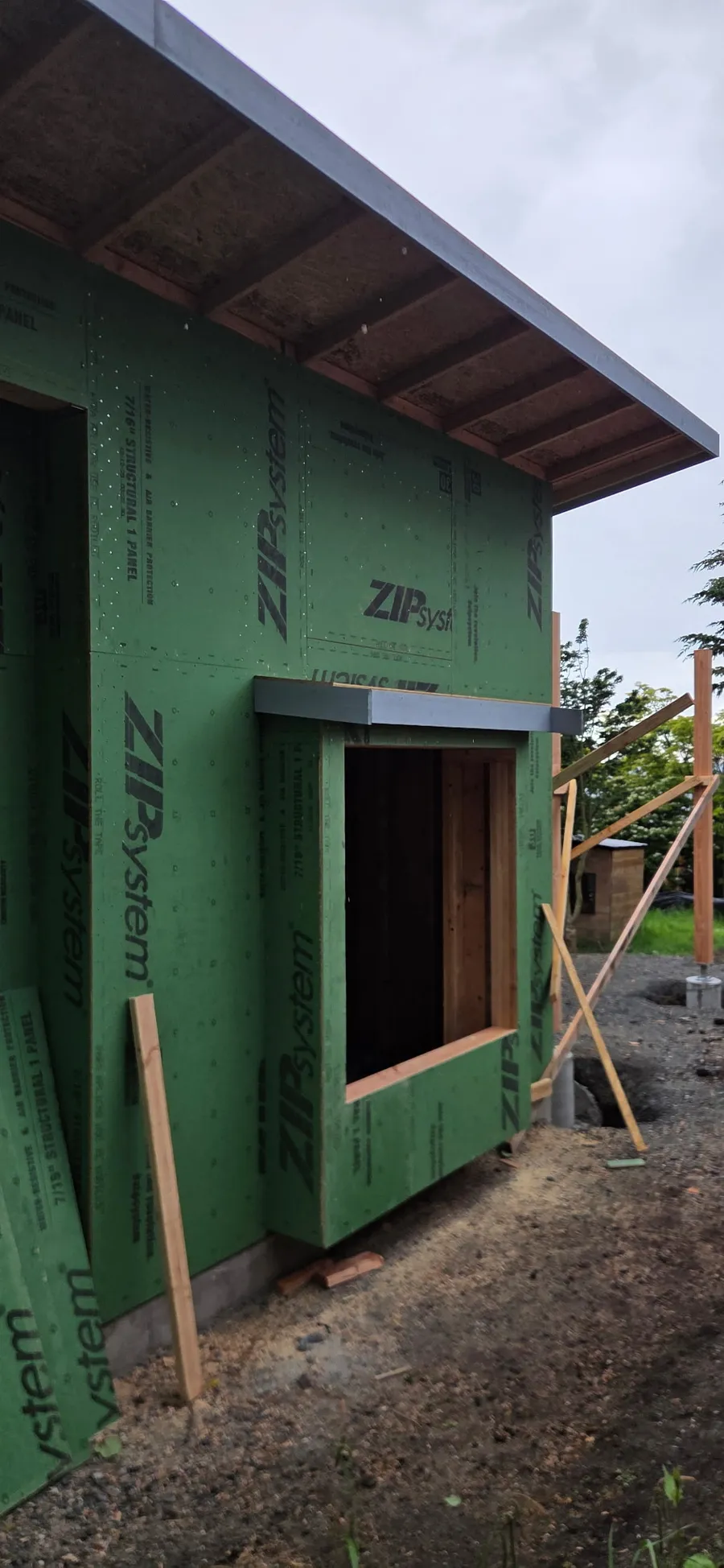 Wall with green ZIP System sheathing, a flashed window opening, and a roof overhang