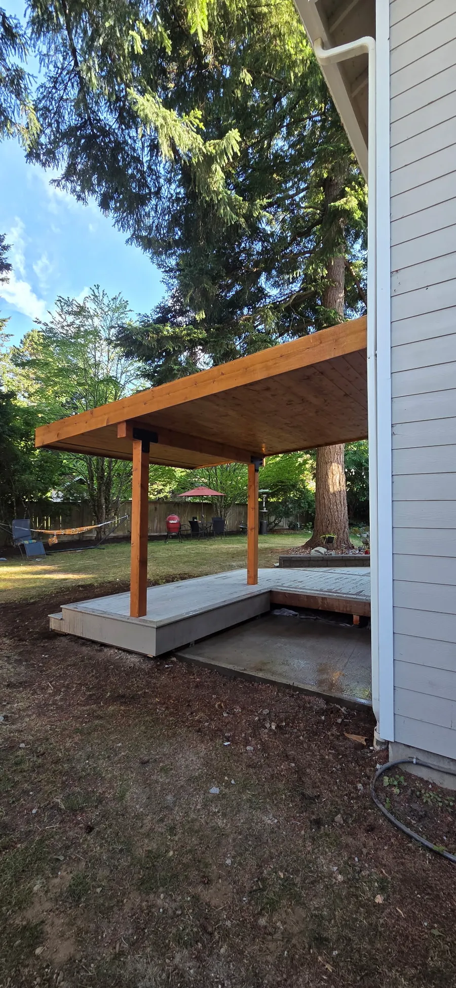 Side view of a covered deck with cedar posts and a stained wood ceiling beside lap siding