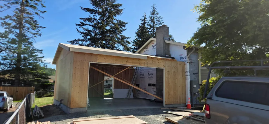 Newly framed garage with plywood walls next to a house wrapped in house wrap