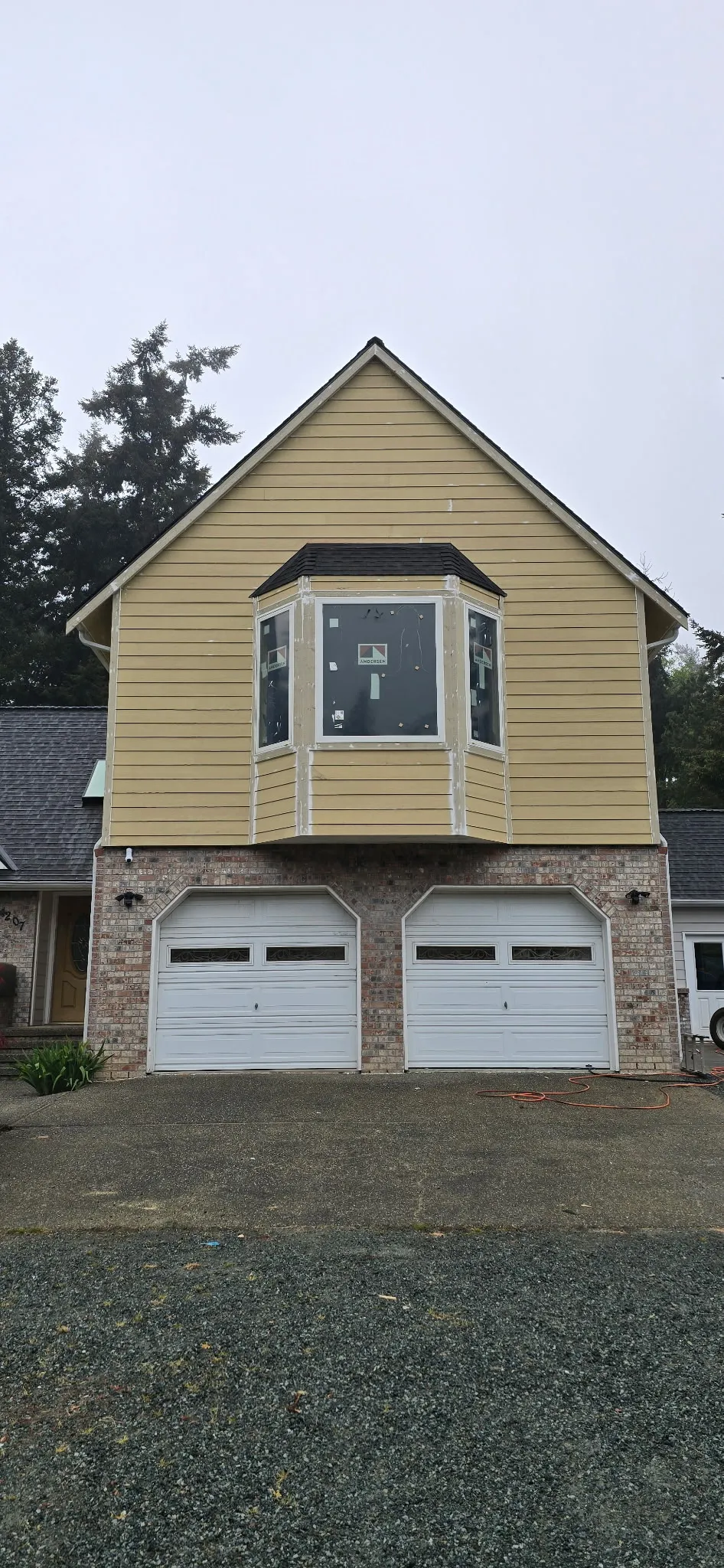 Front of a home with new yellow lap siding, a bay window, and a brick base above a two-car garage