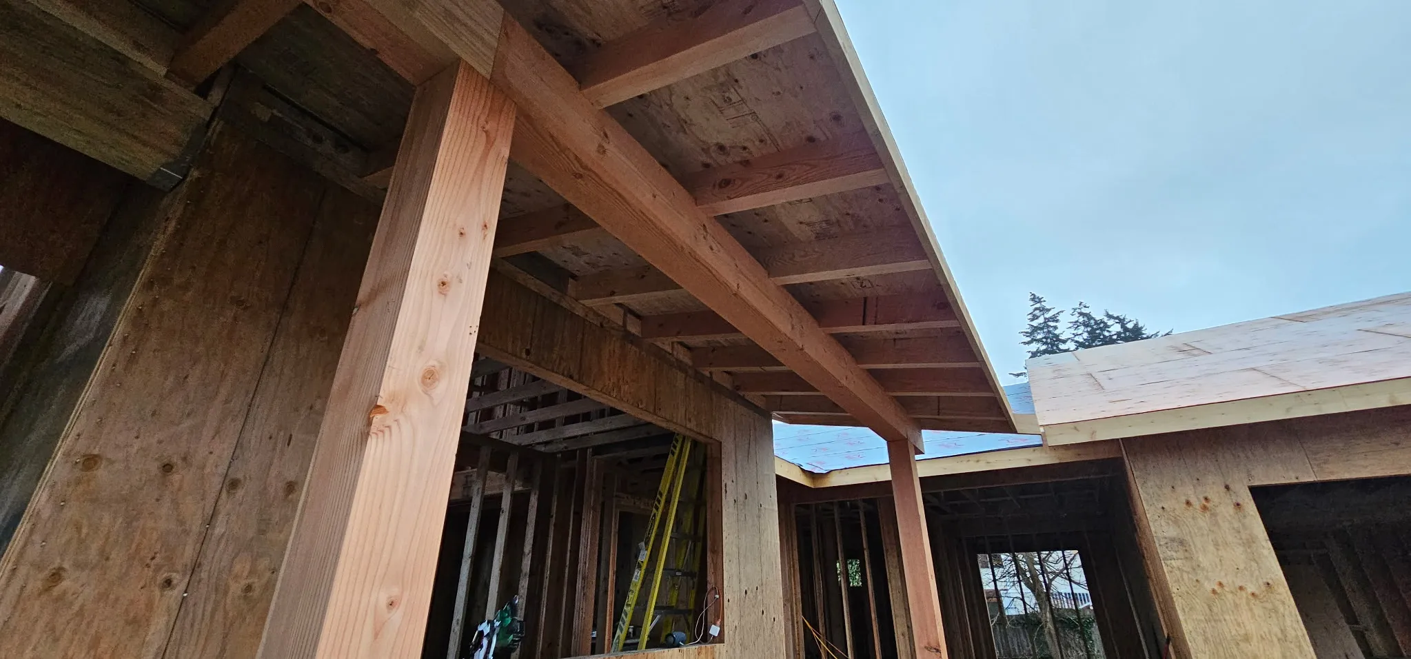 Timber post and beam framing at a covered entry, with a roof overhang and sheathed walls