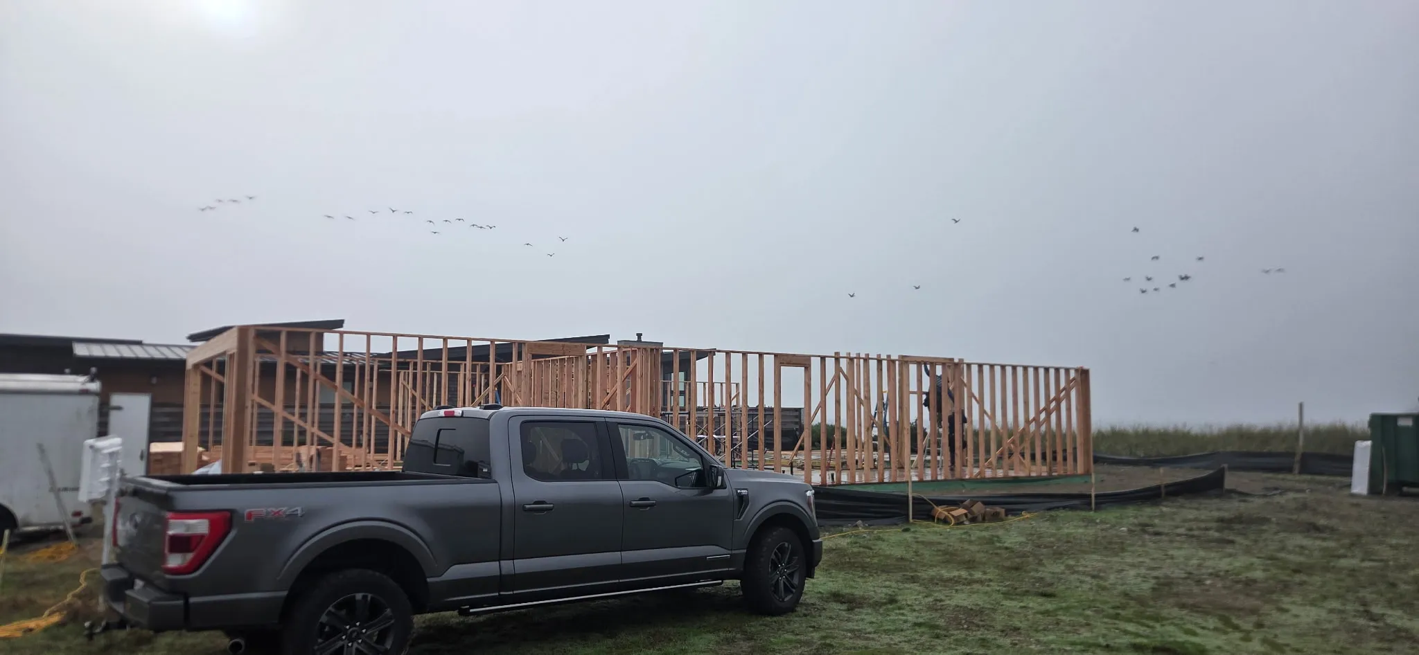 Wall framing for a new single-story building on an open lot, with a pickup truck in front