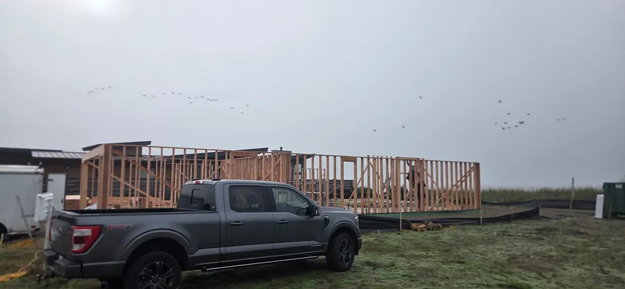 Wall framing for a new single-story building on an open lot, with a pickup truck in front