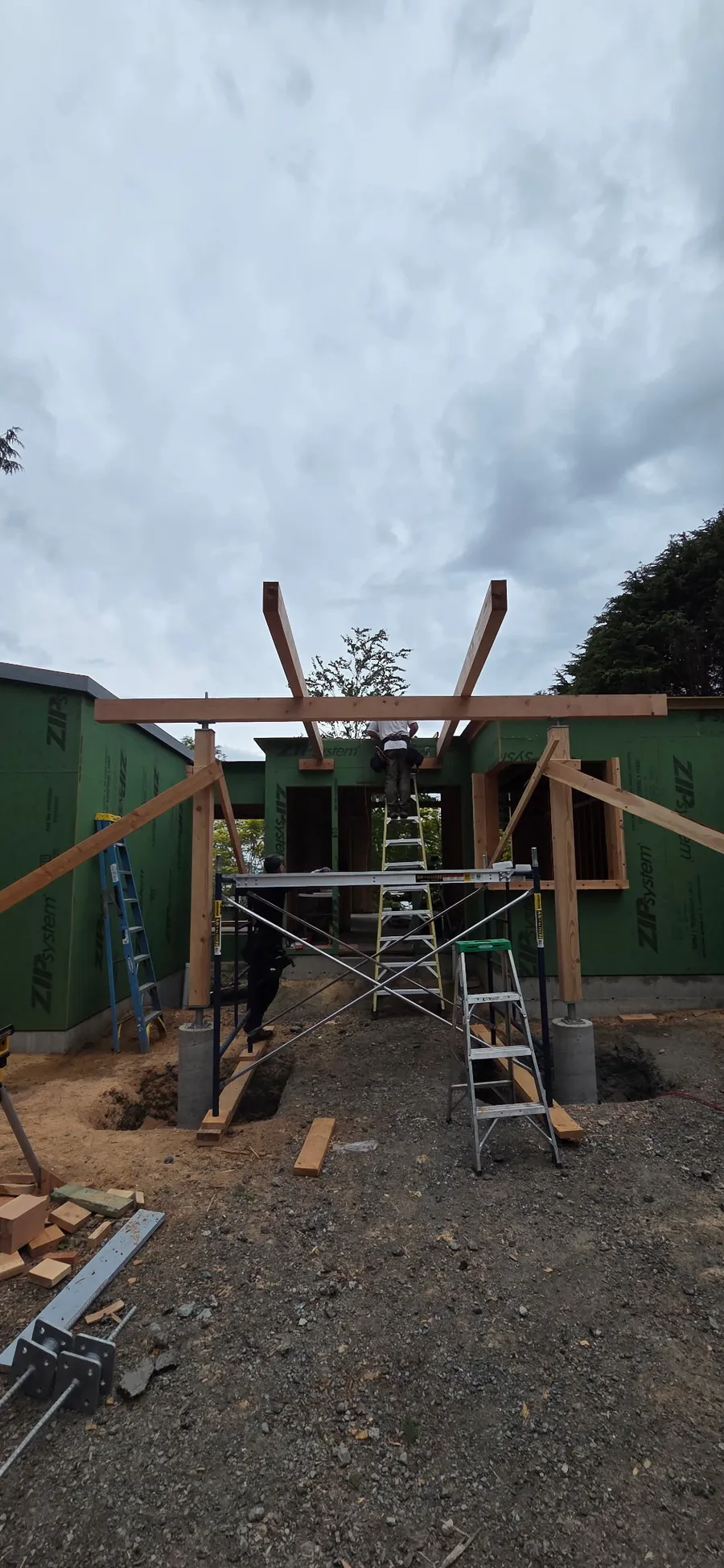 Crew setting a timber beam frame on scaffolding between green-wrapped walls