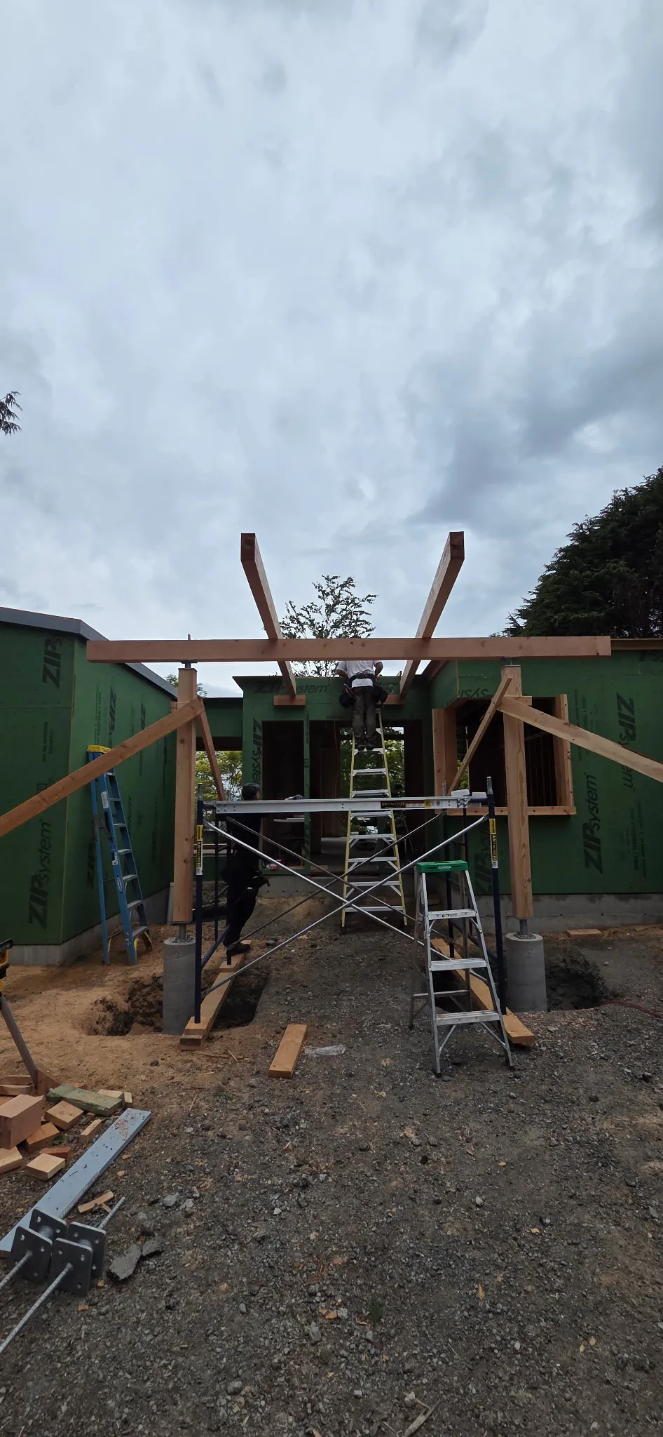 Crew setting a timber beam frame on scaffolding between green-wrapped walls