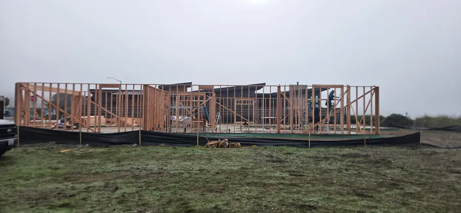Long stretch of wall framing with diagonal bracing on a foundation, with silt fencing around the site