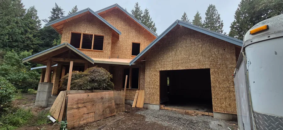 Two-story home framed and sheathed with a garage, gabled roof, and metal roof edge, surrounded by trees