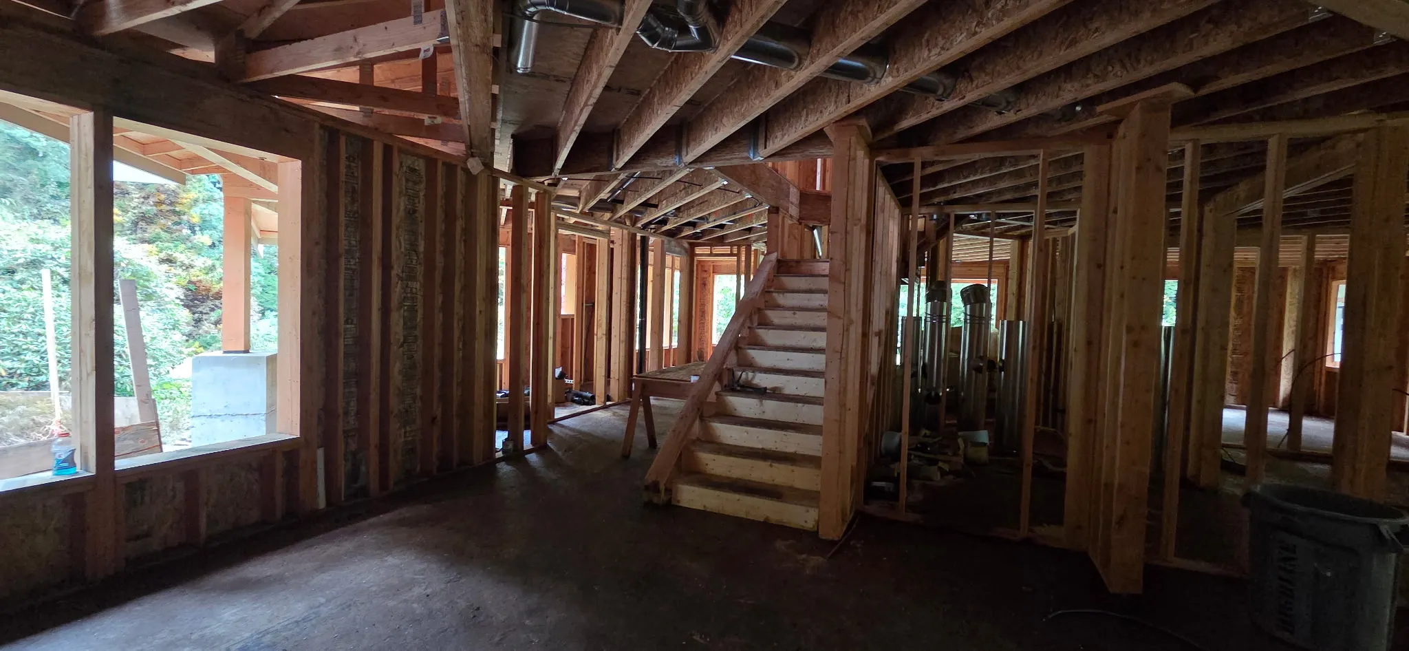 Interior of a framed home with a stairway, ceiling joists, and large window openings