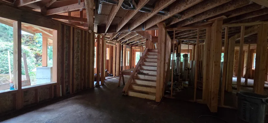 Interior of a framed home with a stairway, ceiling joists, and large window openings