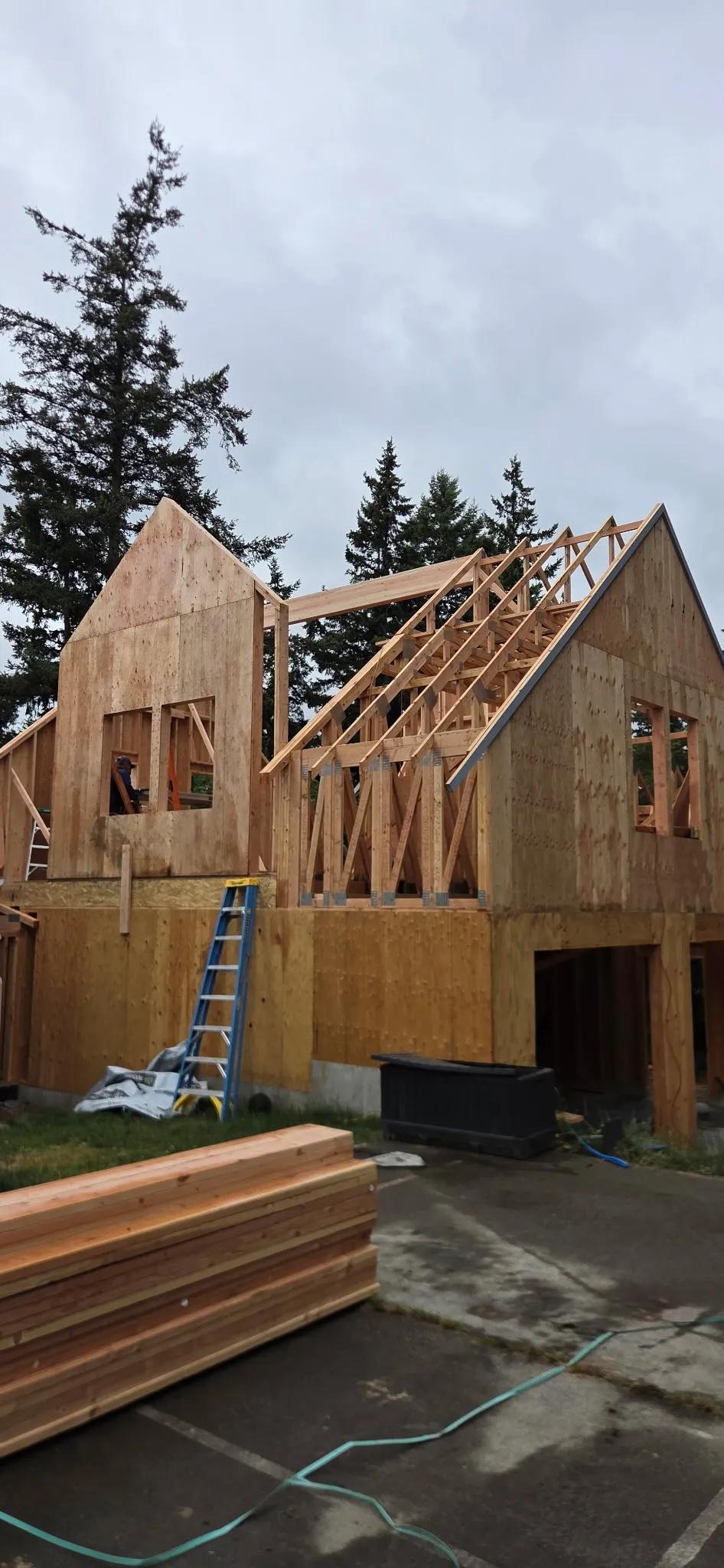 Home under construction with the roof trusses going up on the second floor and lumber stacked in the foreground