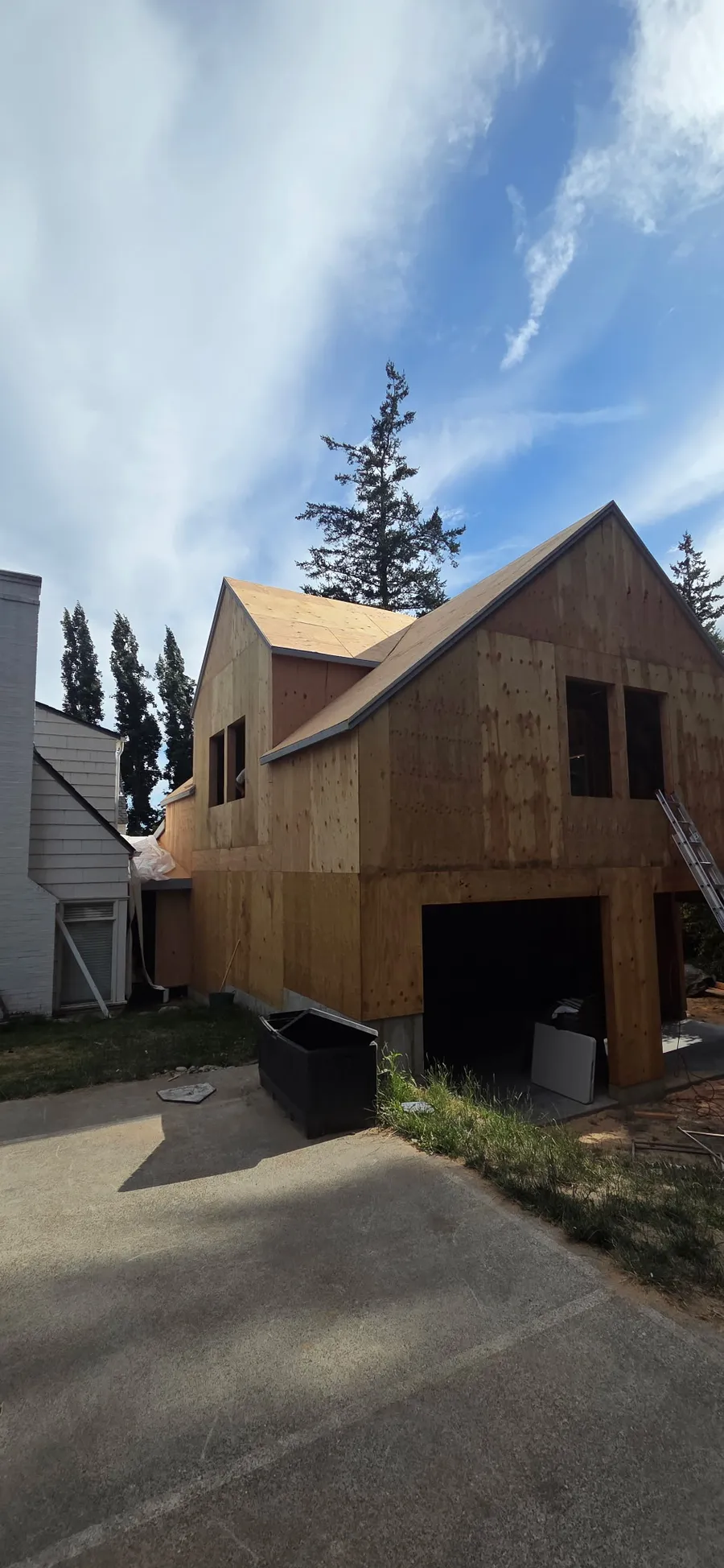 Framed and sheathed home with a garage and gabled roof next to an existing house